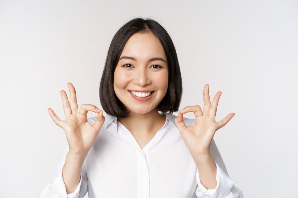 close up head portrait asian girl showing okay ok sign smiling satisfied recommending being pleased praise make compliment white background 1258 89128