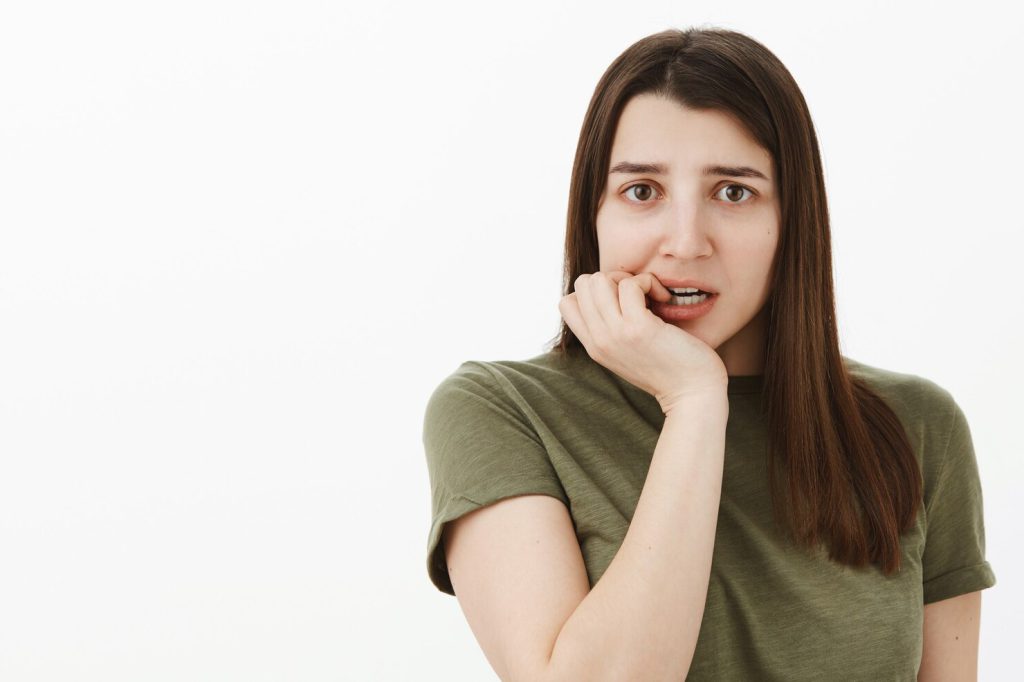 close up shot nervous unsure insecure female coworker messing up documents worried someone notice biting fingernails anxiously frowning standing intense gray wall 176420 22784